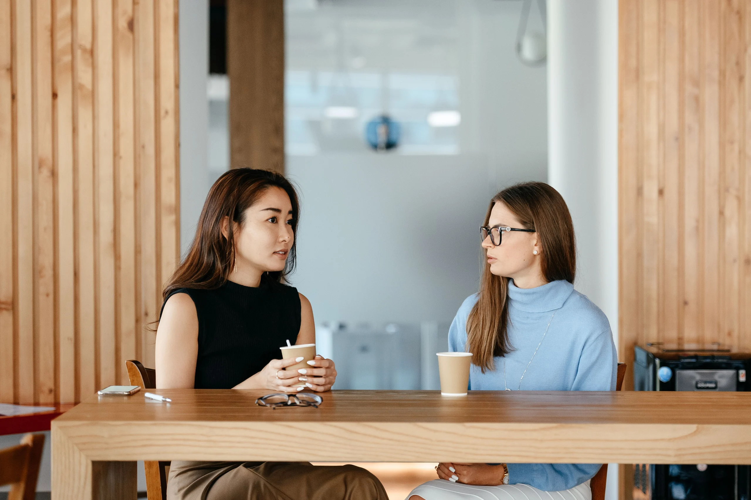 Two women listening and talking across a table over coffee.